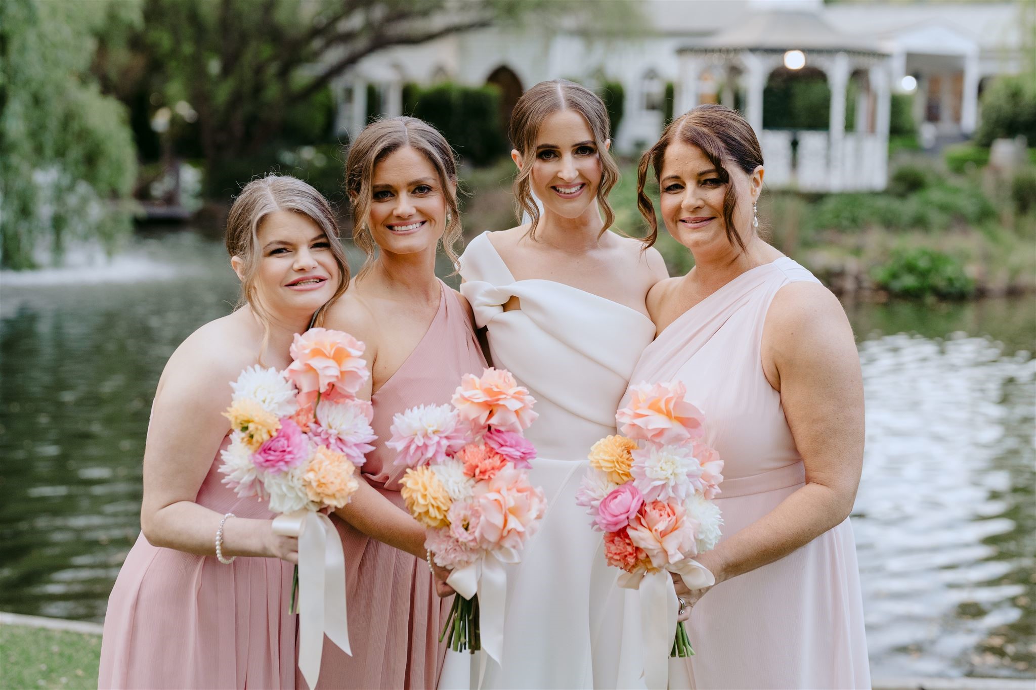 Bride with her three bridesmaids in pink dresses with pastel orange and pink bouquets.